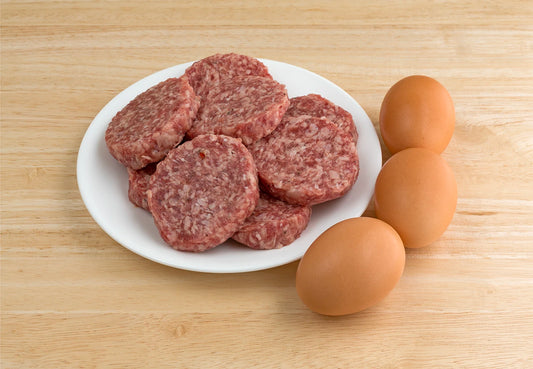 Raw Beef Country Sausage patties on a white plate with three brown eggs on a wooden surface